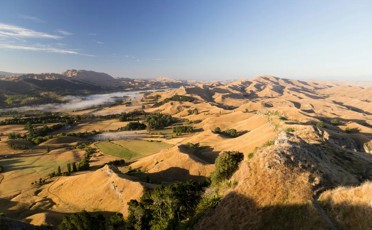 Golden hills, green fields, and low mist beneath a blue sky.